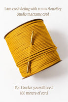 A spool of mustard yellow crocheting cord wrapped diagonally, with a gold crochet hook resting on top. Text on a white background reads: 'I am crocheting with 6 mm MonoMey Studio macrame cord' and 'For 1 basket you will need 100 meters of cord'.